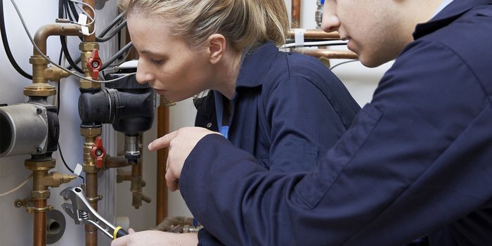 Eine Frau und ein Mann arbeiten konzentriert an einer Rohrleitung, während sie Werkzeuge in der Hand halten.