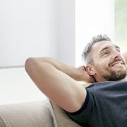 Ein Mann der auf dem Sofa liegt mit den Haenden hinterm Kopf 