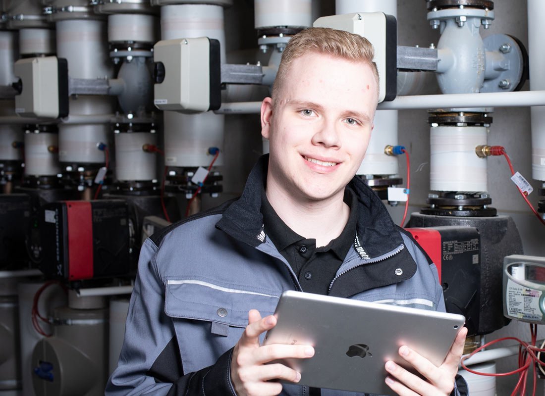 Ein junger Anlagenmechaniker vor einer Heizungsanlage, der ein Tablet hält 